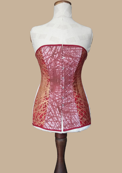 Corset. Front view. White cotton dyed red and red fine wool screen printed with cross linear pattern in copper and red tones, red cotton drill, steel split busk, steel spiral boning and rigilene boning.