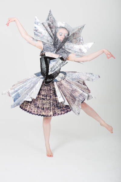 Costume for a Will-o-the-wisp in Faust. Handmade. Partlet with restrictive collar, pleated collar wired around partlet collar, bodice with hip fins and pleated hip skirt, pleated domed skirt over pocket hoops. Tones of black, silver, blue patterning. Front  view. Performer: E. Phillips (female).